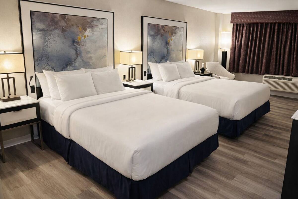 A hotel room with two beds, a desk, a chair, two lamps, and a large abstract painting on the wall.