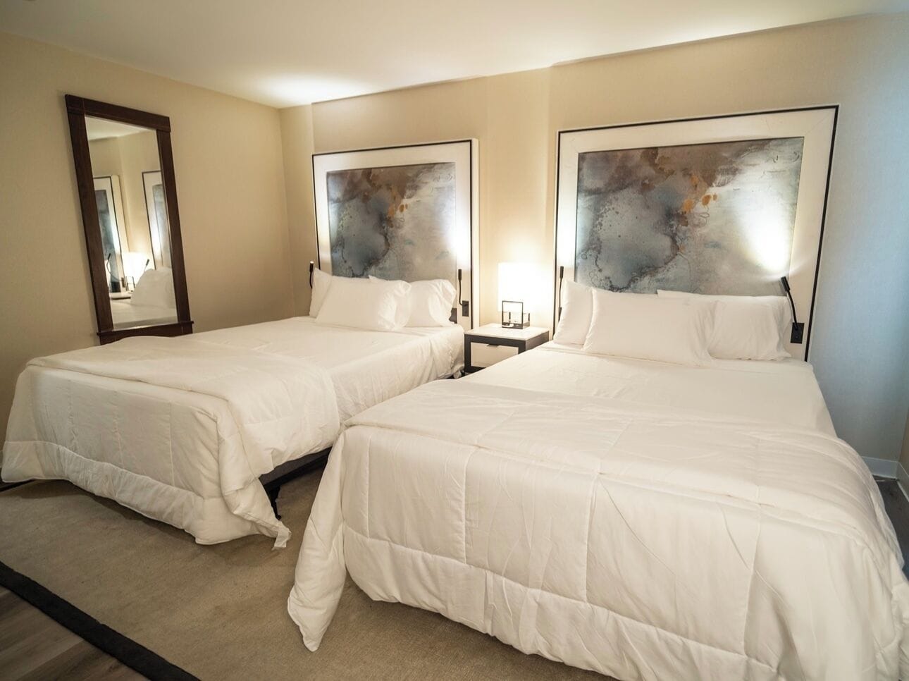 A hotel room with two beds, a large mirror, and abstract wall art.