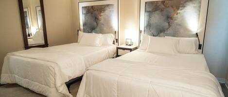 A hotel room with two beds, a large mirror, and abstract wall art.