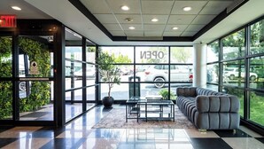 Un vestíbulo con piso a cuadros, mostrador de recepción, zona de estar y amplias ventanas que dan a la vista de automóviles estacionados y follaje exterior.