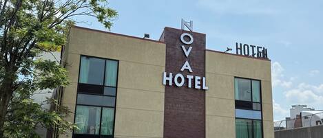El exterior del Hotel Nova, con un letrero visible, estacionamiento y una fachada de edificio moderna.