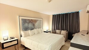 Una habitación de hotel con una cama grande, un escritorio, una silla, un sofá y un ventanal con cortinas.