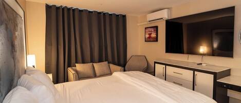 Habitación de hotel con una cama grande, un escritorio con silla, un televisor de pantalla plana y una ventana con cortinas.