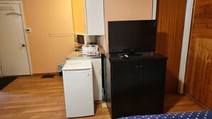 A compact kitchen with a refrigerator, microwave, and a black cabinet with a television.