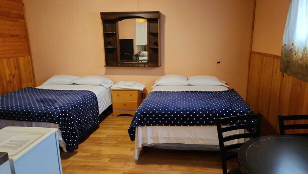 A room with two beds, wooden flooring, a small table, and a mirror on the wall.