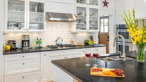 A modern kitchen with white cabinetry, a stainless steel range hood, and a black countertop.