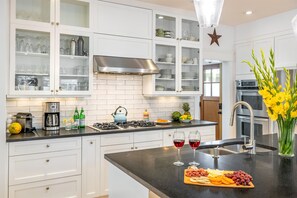 A modern kitchen with white cabinetry, a stainless steel range hood, and a black countertop.