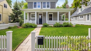 A two-story house with a front porch, a mailbox, and a white picket fence.