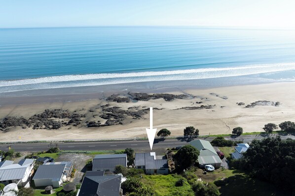 An aerial view of a coastal area with a beach, rocky outcrops, and residential buildings.