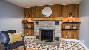 A living room with a stone fireplace, wooden shelves, a black leather chair, and patterned floor tiles.