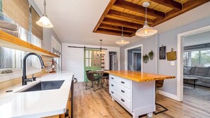 A modern kitchen with a wooden island, white cabinetry, and a farmhouse-style ceiling.