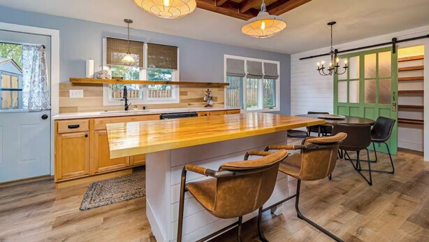 A modern kitchen with a large island, wooden cabinets, and pendant lighting.