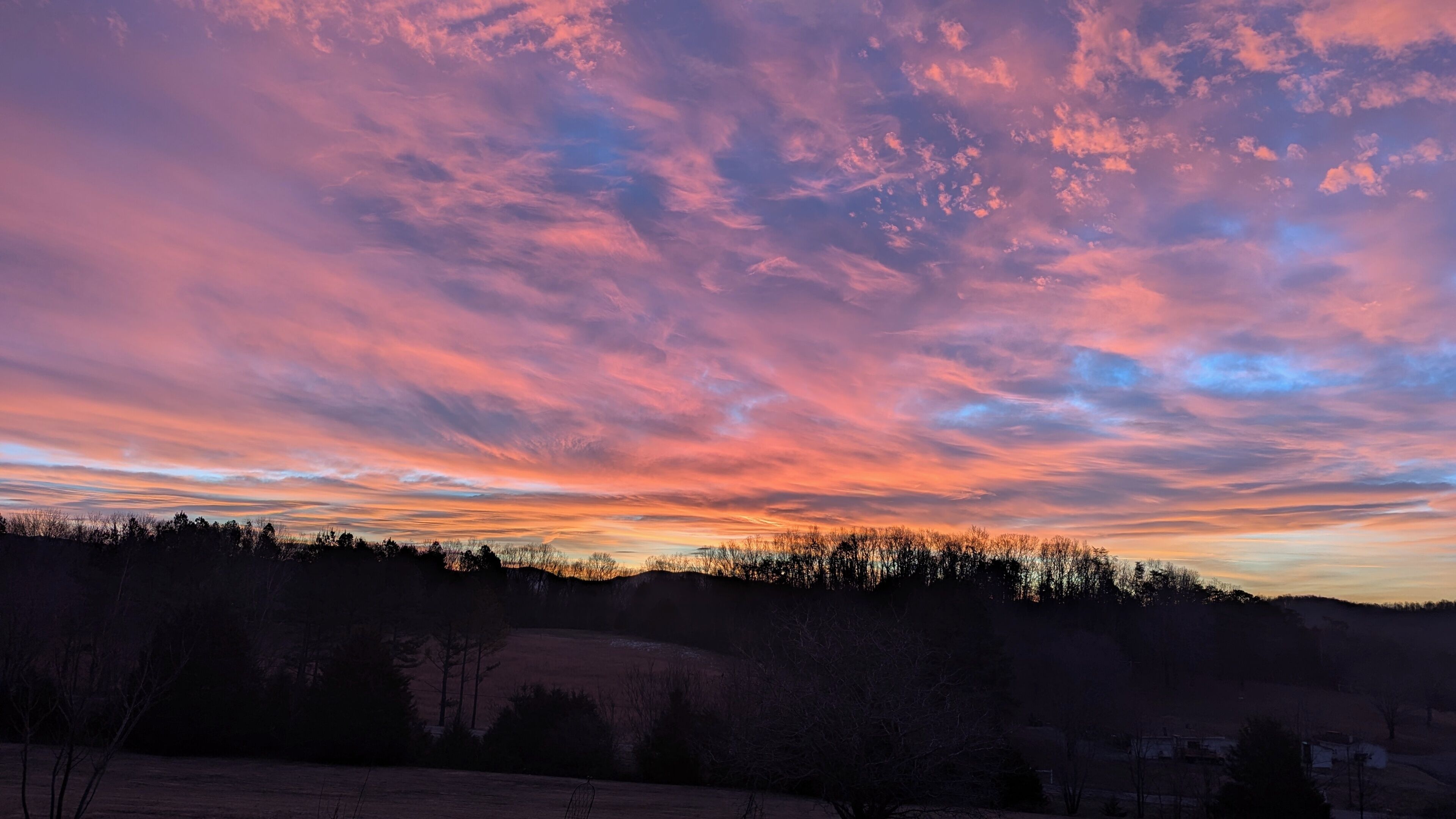 A landscape with a sunset sky, a silhouette of trees, and a distant hill.