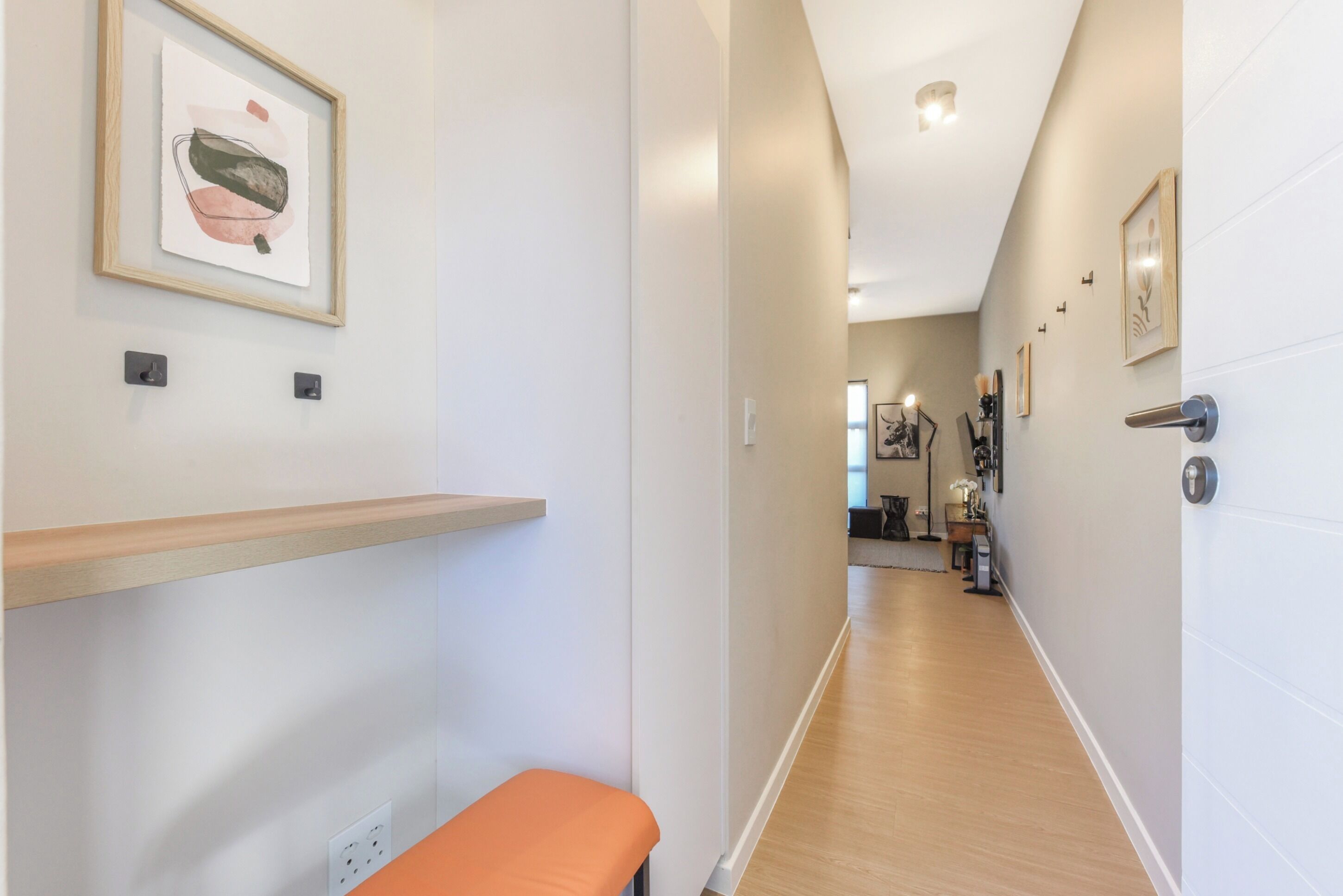 A hallway with a bench, a framed artwork on the wall, and a door with a handle.