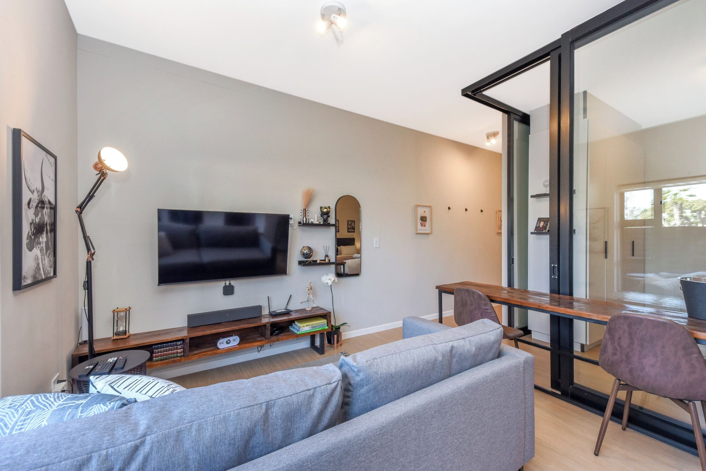 A modern living room with a flat-screen TV, a sofa, a coffee table, and a dining area with a glass partition.