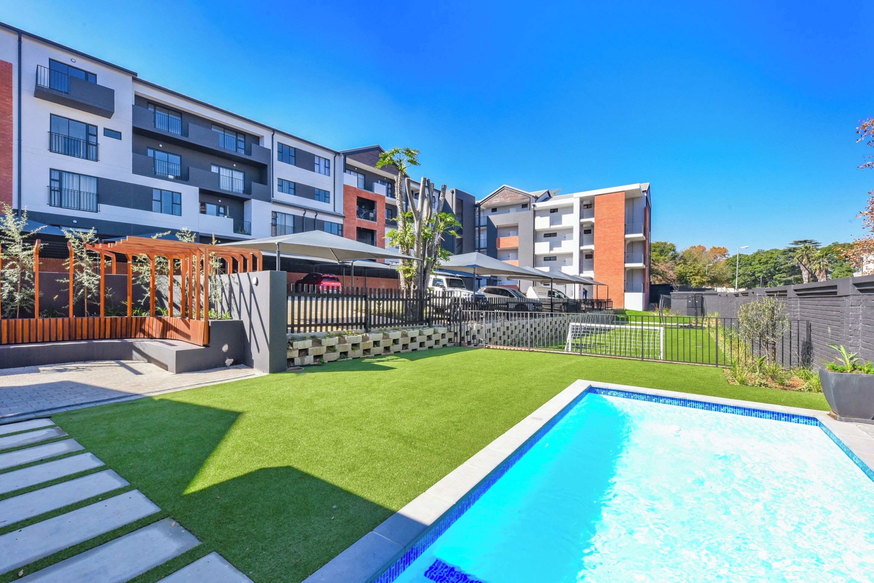 A modern apartment complex with a swimming pool, outdoor seating area, and a well-maintained lawn.