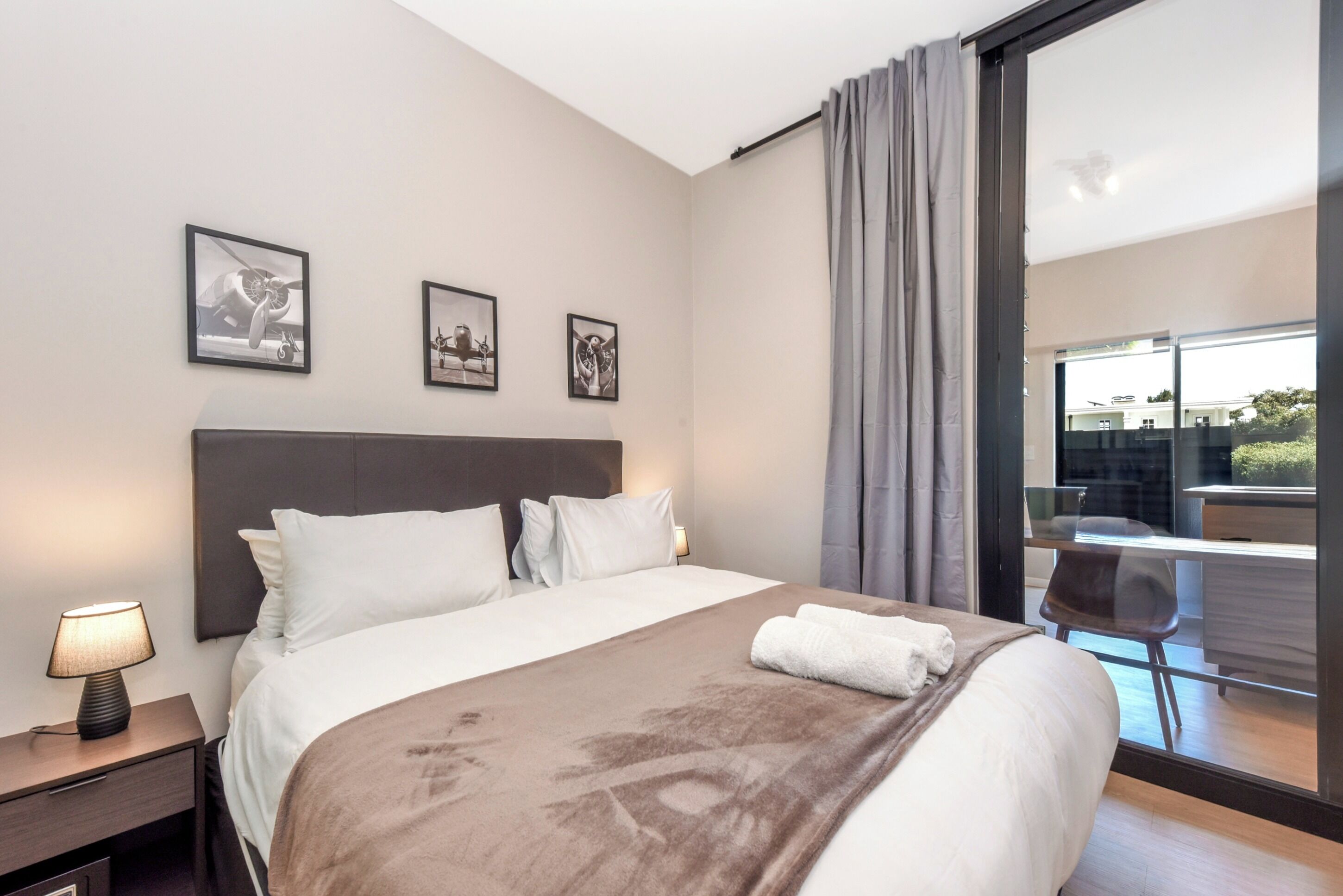 A modern hotel room with a large bed, a desk, and a balcony with a view.