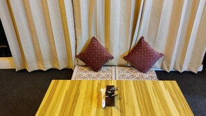 Una habitación con una mesa de madera, dos cojines estampados y una cortina de rayas verticales.