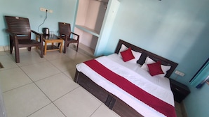 Un dormitorio con cama, dos sillas, una mesita y una tetera.