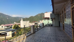 Un balcón con baldosas de diseño, baranda metálica y vistas a edificios y montañas al fondo.