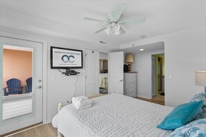 A bedroom with a bed, a ceiling fan, a television mounted on the wall, and a door leading to a bathroom.