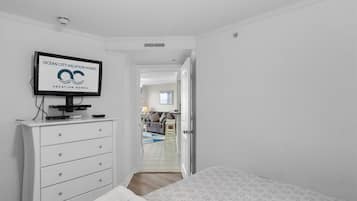 Ein Schlafzimmer mit einem Bett, einem Fernseher auf einer Kommode, einer weißen Kommode und einer Tür zu einem Wohnbereich.