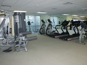 A gym with cardio machines, weight machines, and a wall-mounted TV.