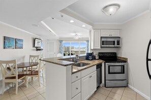A kitchen with white cabinets, a black stove, a microwave, and a refrigerator. There is a dining area with a table and chairs.