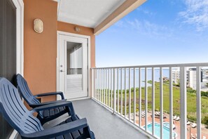Un balcón con dos sillas azules, una puerta blanca y vistas a una piscina y vegetación.