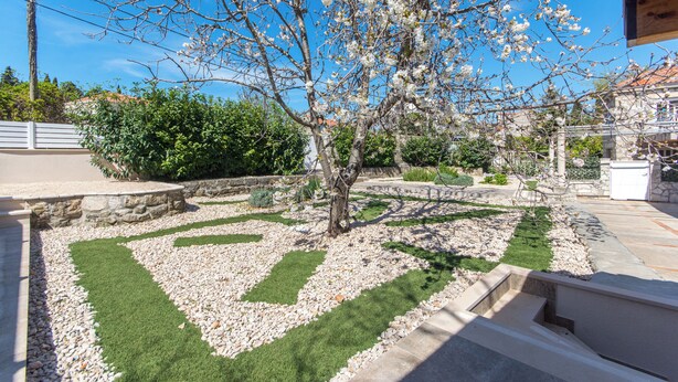 Un jardín ajardinado con un árbol, un muro de piedra y una zona pavimentada.