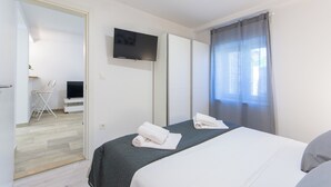 Habitación de hotel con una cama, un televisor montado en la pared y una ventana con cortinas.