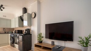 Moderni keittiö, jossa on kodinkoneet, sekä ruokailutila, jossa on televisio ja viihdekeskus.