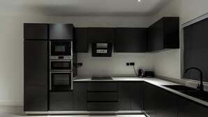 Una cocina moderna con armarios negros, horno integrado y un lavamanos.