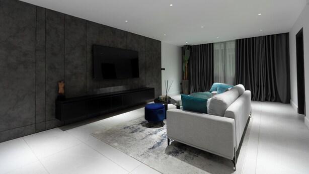 Una sala de estar moderna con un televisor de pantalla plana montado en una pared oscura, un sofá blanco con cojines color turquesa y un pequeño taburete azul.