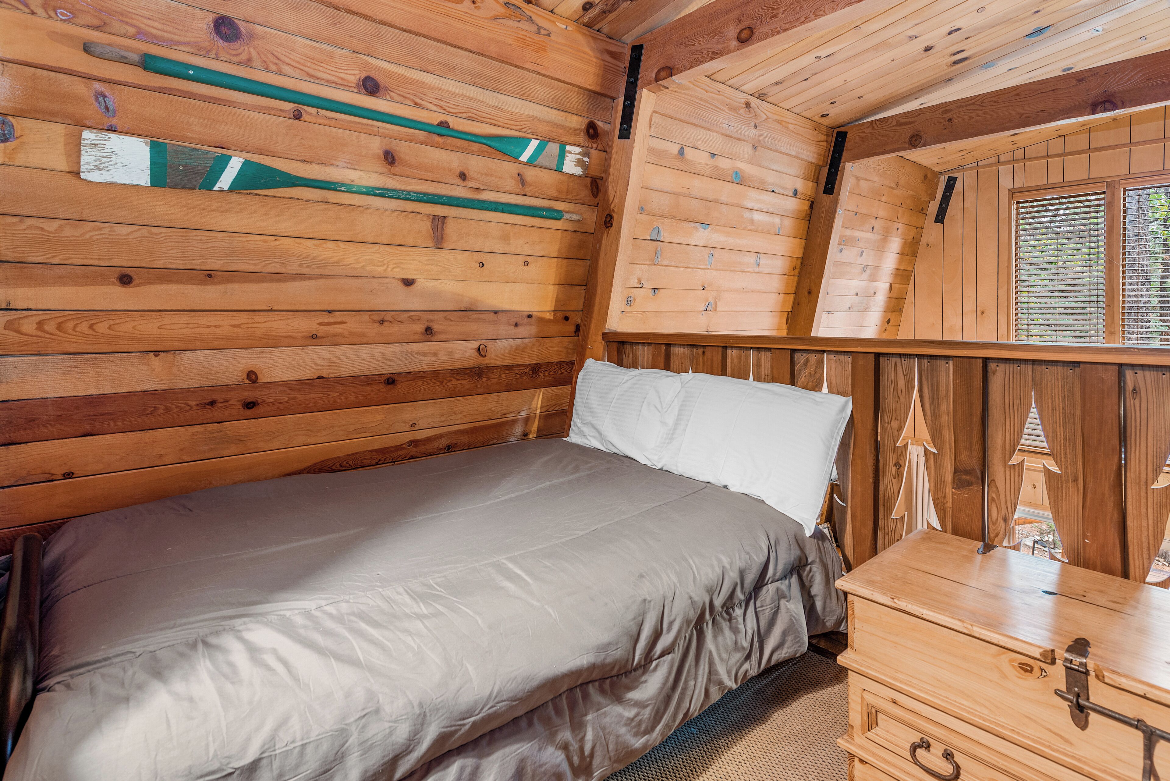 Habitación de cabaña de madera con cama, cómoda y ventana con persianas.