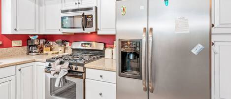 Una cocina con armarios blancos, un refrigerador de acero inoxidable, un microondas, una estufa y una cafetera.