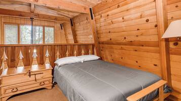A wooden cabin bedroom with a bed, dresser, and window with blinds.