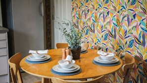 A round wooden dining table with white plates and bowls, a woven basket with a plant, and two salt and pepper shakers. - Crookes Gem with Garden & Alpacas Nearby (Sheffield)