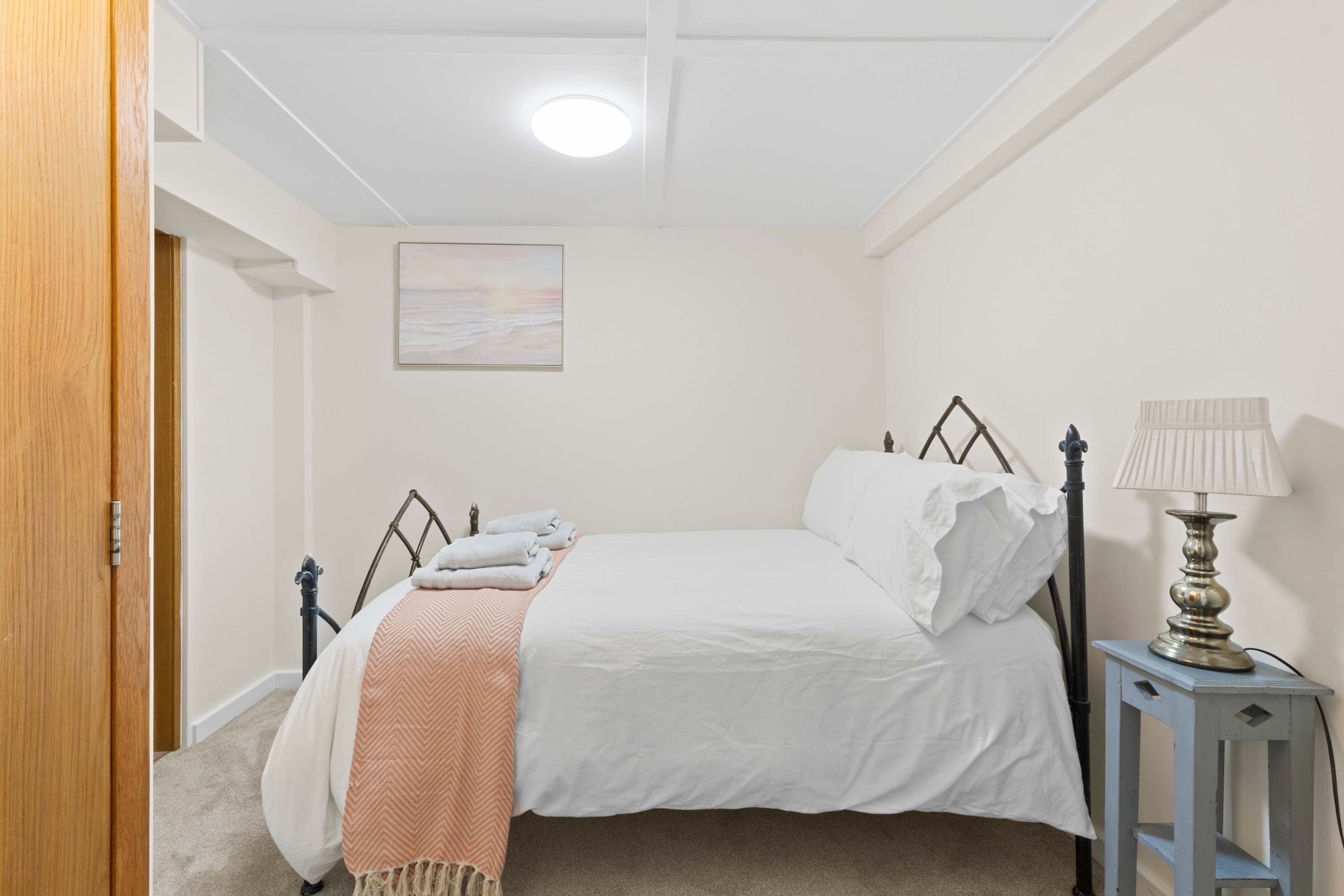 Een slaapkamer met een bed, een bedlamp en een schilderij aan de muur.