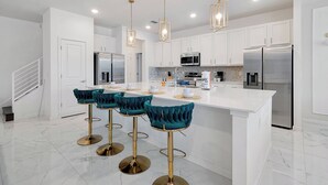 Une cuisine moderne avec des meubles blancs, des appareils en acier inoxydable et un îlot central doté de tabourets de bar.