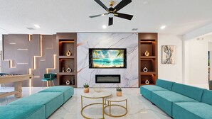 Un salon moderne avec des canapés de couleur turquoise, une table de billard et un téléviseur fixé sur un mur en marbre.