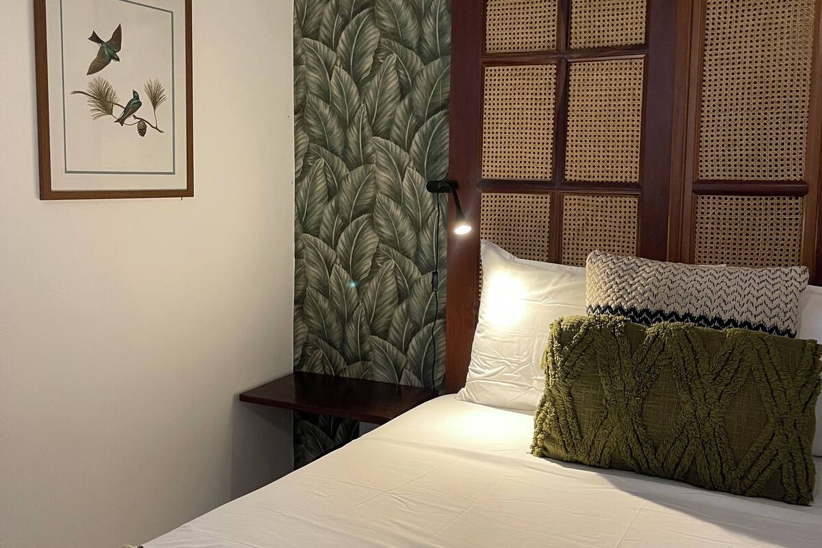 A neatly made bed with a striped blanket, a framed picture of birds on the wall, and a textured leaf-patterned wallpaper.