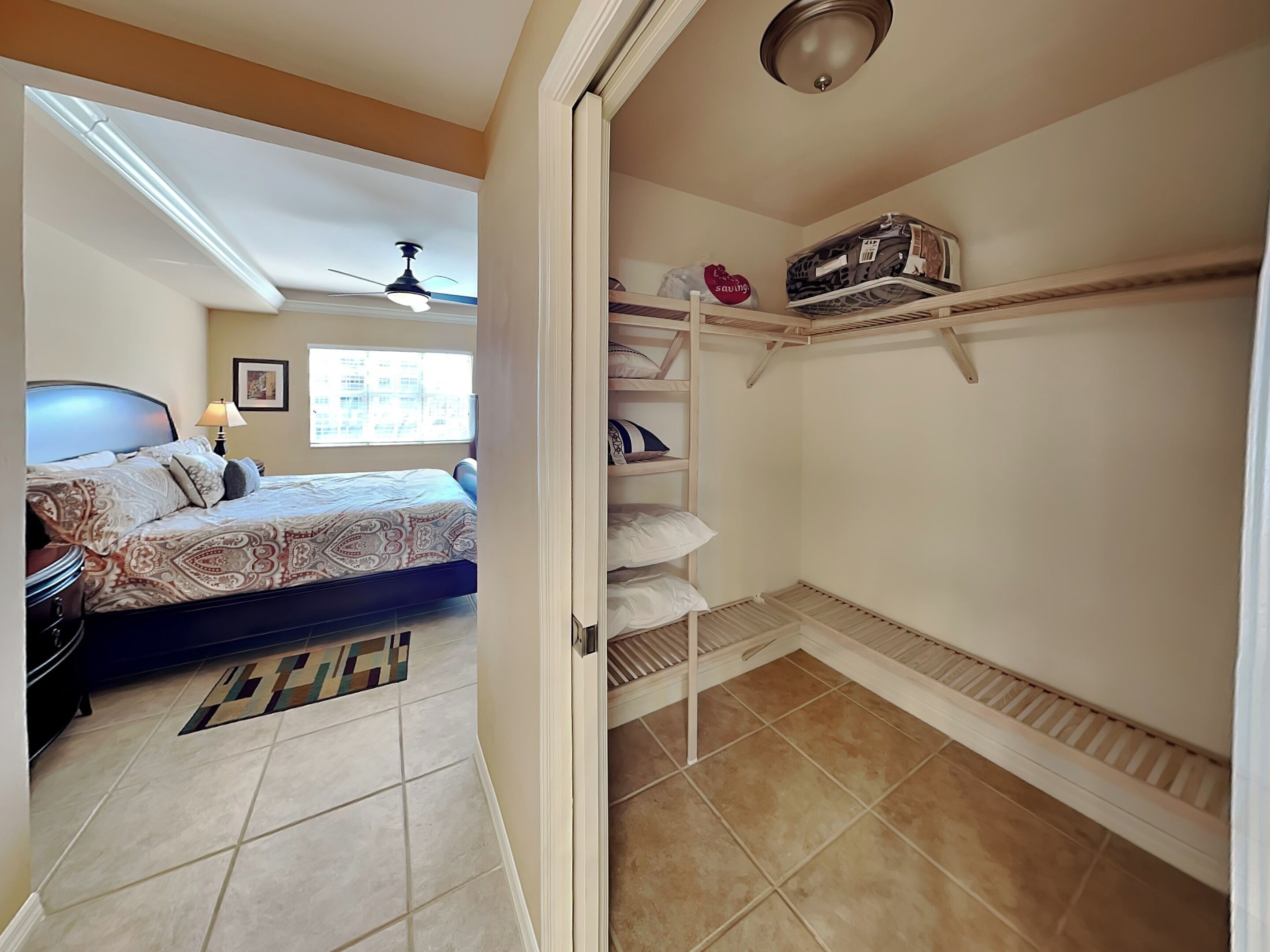 Un dormitorio con cama, ventilador de techo, ventana y armario con estantes.