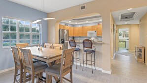 Una cocina moderna con armarios de madera, un refrigerador de acero inoxidable y una zona de comedor con mesa y sillas de madera.