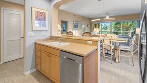 A modern kitchen with a built-in dishwasher, wooden cabinets, and a dining area with a table and chairs. - Bella Lago 324 by Distinctive Beach Rentals (Fort Myers Beach)