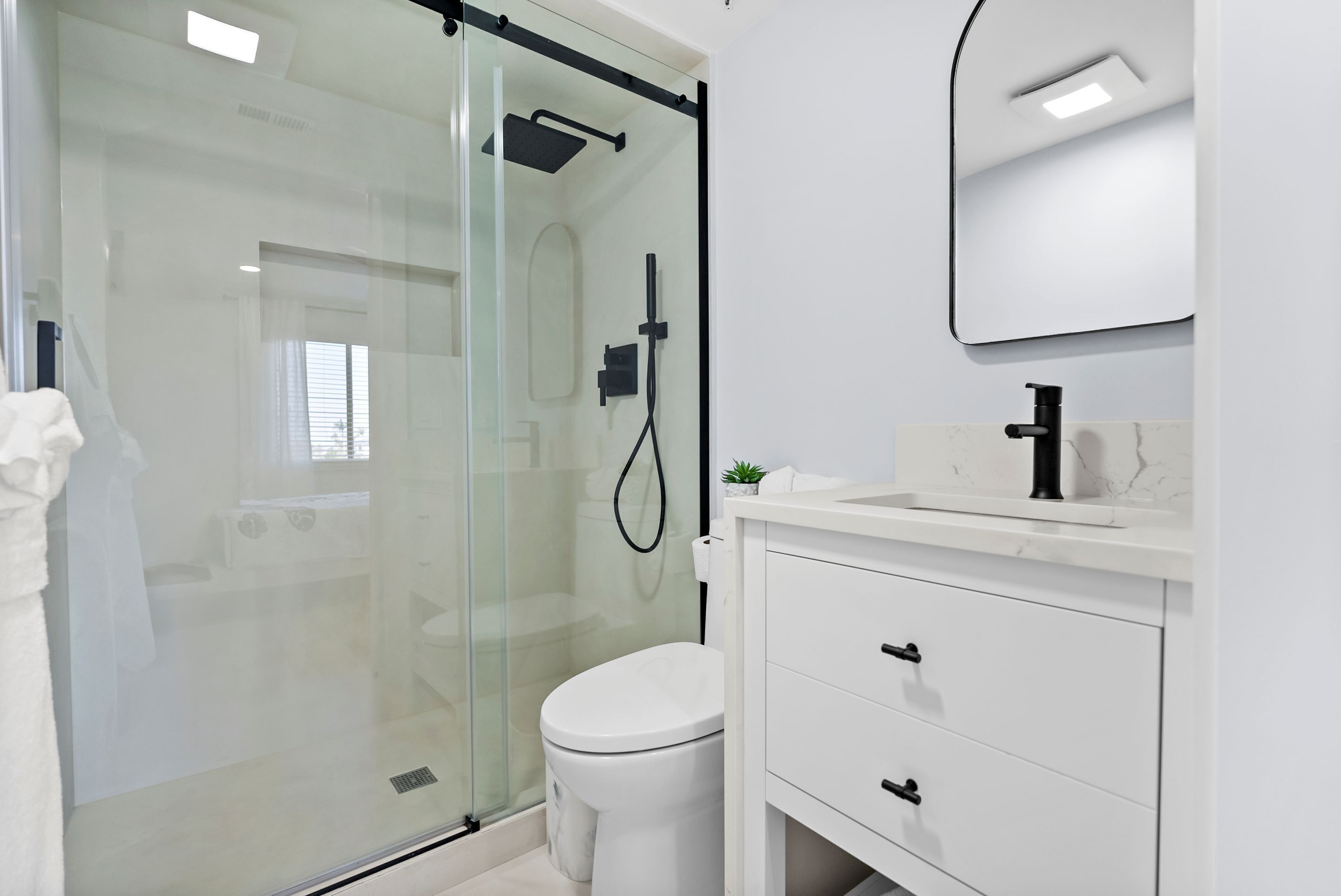 A modern bathroom with a glass-enclosed shower, a white toilet, and a white vanity with drawers.