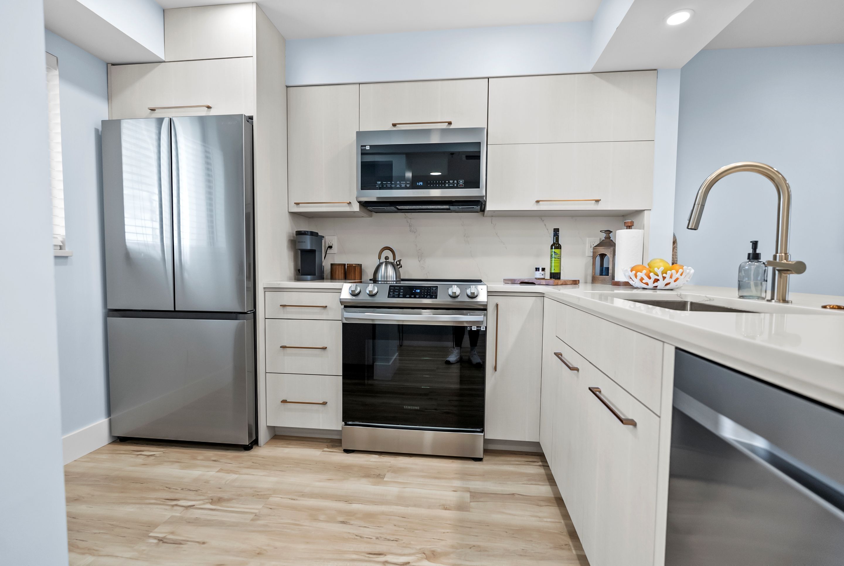 A modern kitchen with stainless steel appliances, white cabinetry, and a wooden floor.