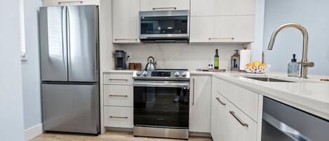 A modern kitchen with stainless steel appliances, white cabinetry, and a wooden floor.