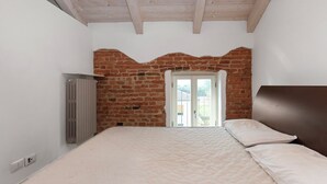 Un dormitorio con pared de ladrillo, un radiador, una cama y una ventana.