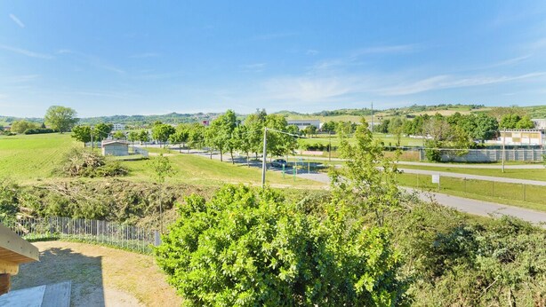 Zona residencial con cielo despejado, campos verdes y una carretera con valla.